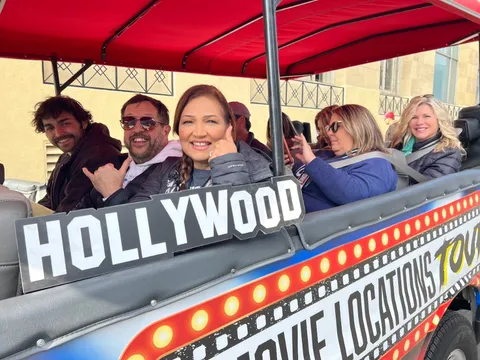 Guests enjoying the Film Freak Movie Locations Tour — holding a Hollywood sign prop on the open-air van